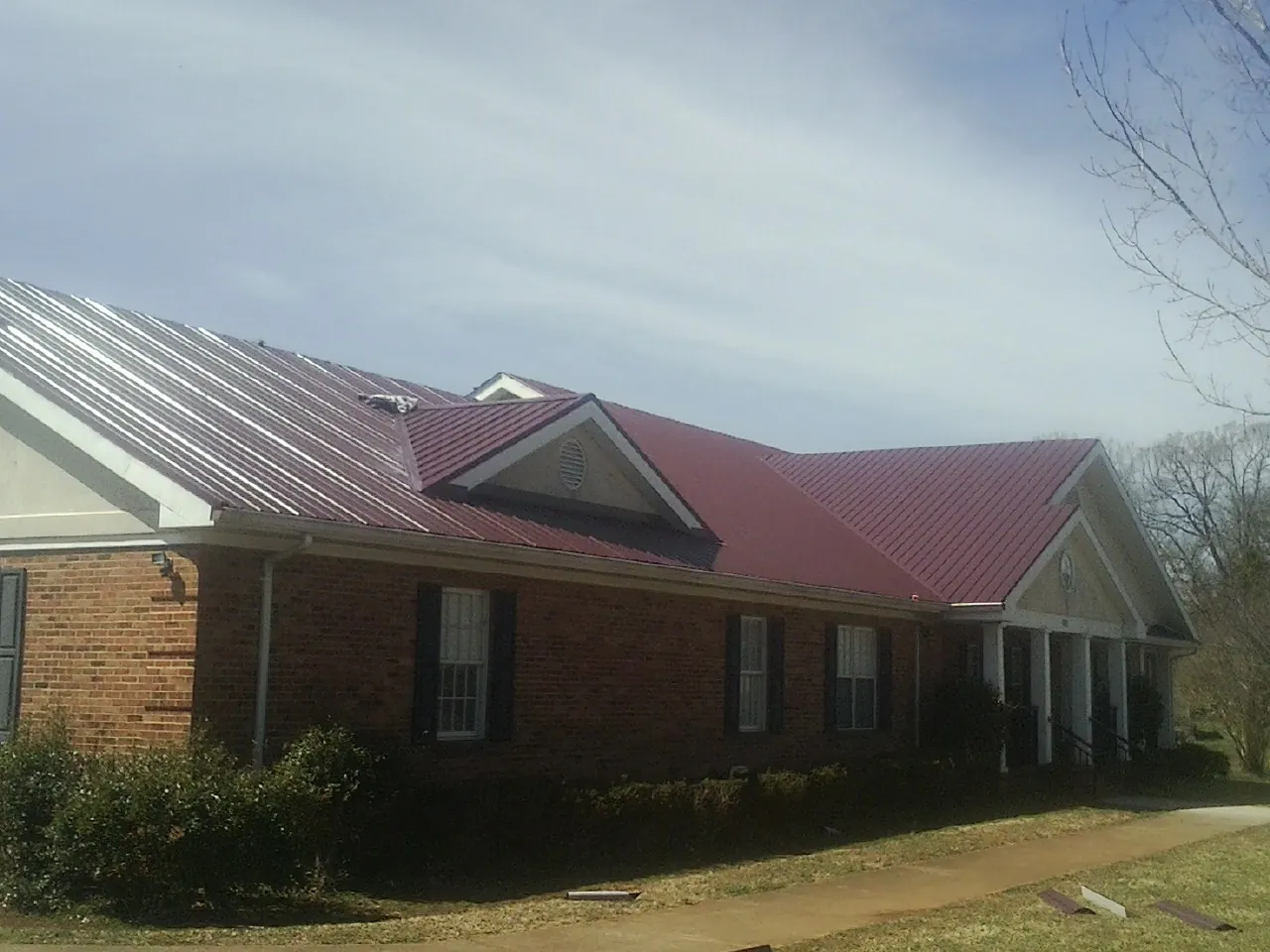 Red metal roof with gabled entries on a long brick building, from a Hail Damage Roof Repair job in Waco