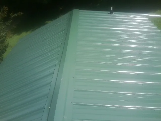 New green metal panels meeting at the ridge of a roof — Flat Roof Repair work by our crew in Waco